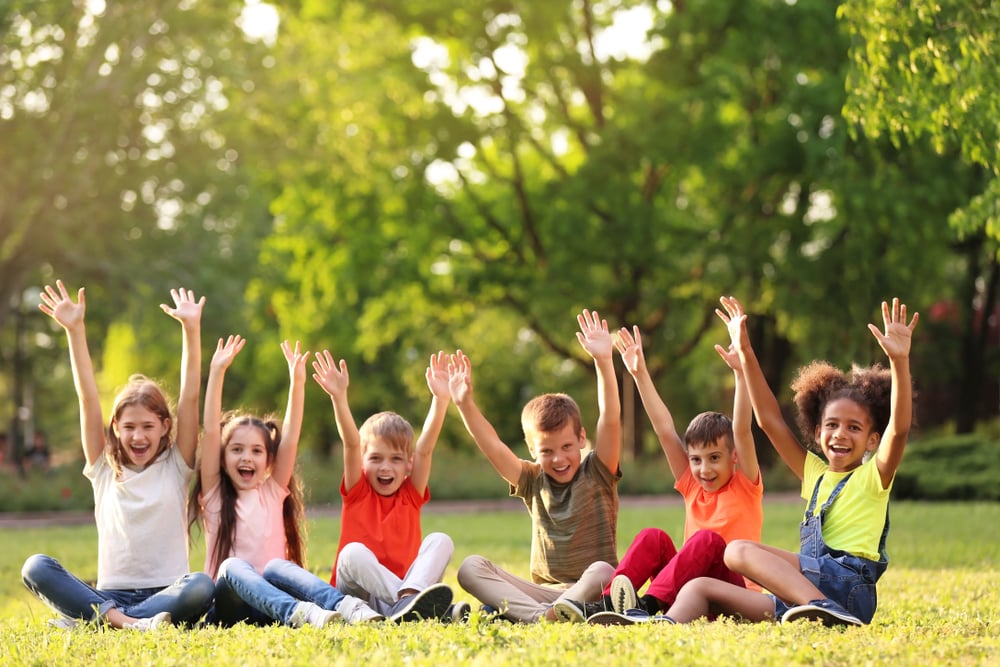 a group of children sitting in a field and raising their hands in excitement